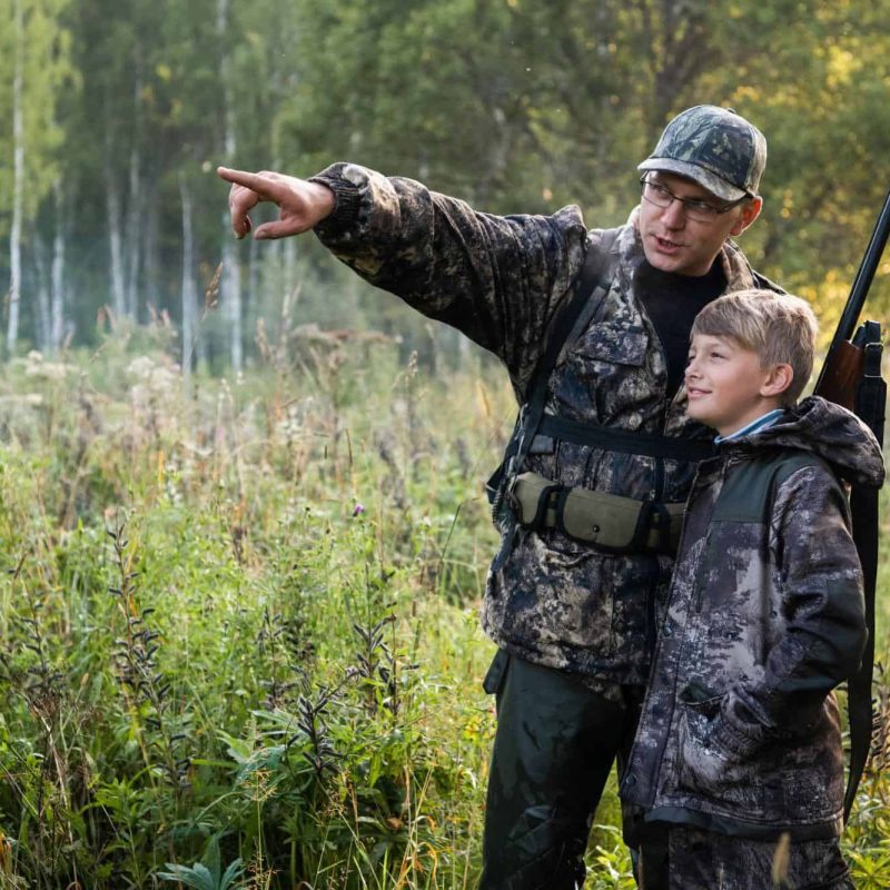 father with gun showing something to son while hunting