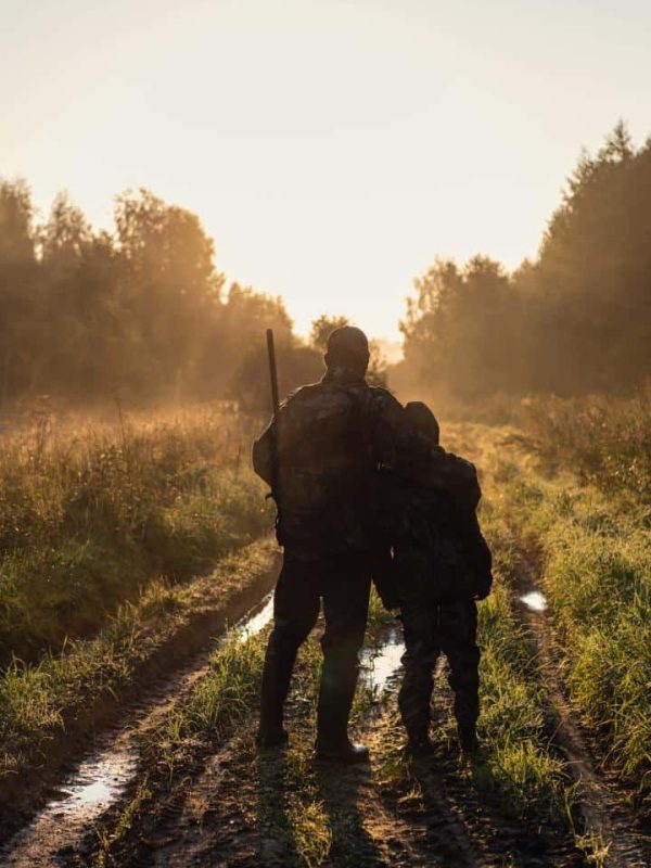 hunters with hunting equipment standing on path in woods